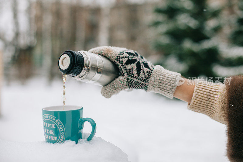 woman hands pours hot tea or coffee out of thermos on winter forest background. girl using a thermos in on a snowy mountain. red cup